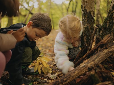 Two children playing with leaves in the forest