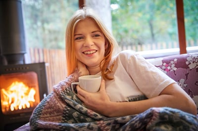 Woman relaxing next to the log burner at Forest Holidays