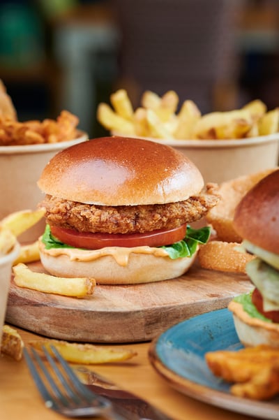 Close up of a chicken burger with cheese, tomato, lettuce and chips