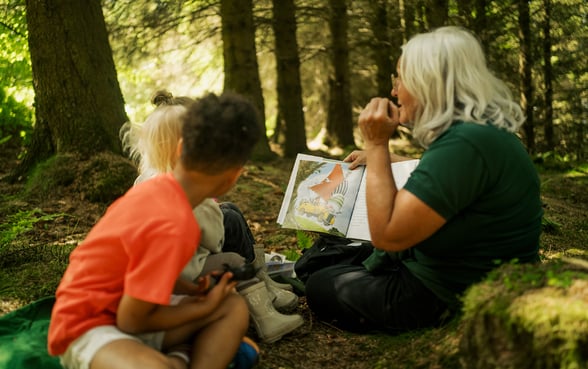 A forest ranger reading a story to children in the forest