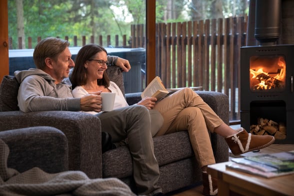 A couple relaxing in front of a log burner at Forest Holidays
