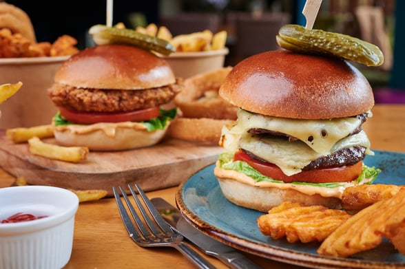 Two burgers with gerkins, onion rings and chips