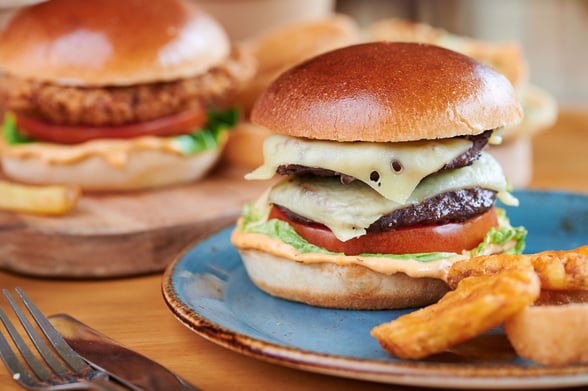 Close up of a beef burger with cheese, tomato, lettuce and chips