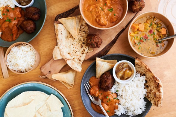 Flatlay photo of indian curries, rice, poppadoms and naan