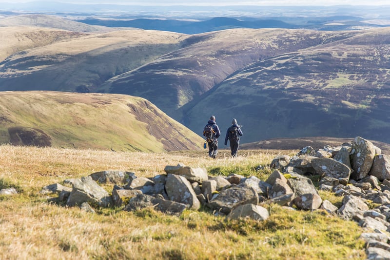 Two walkers descend from a moorland hill top. 
