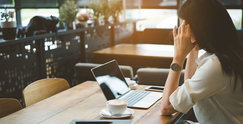 A woman sits with her hands resting on her forehead looking at a laptop screen