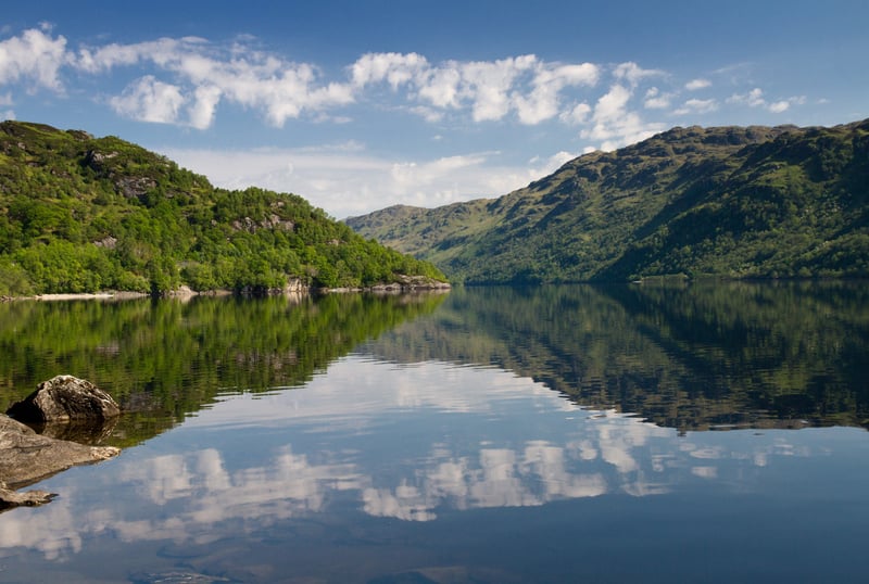 Reflections of trees and clouds on Loch Lomond in Scotland.