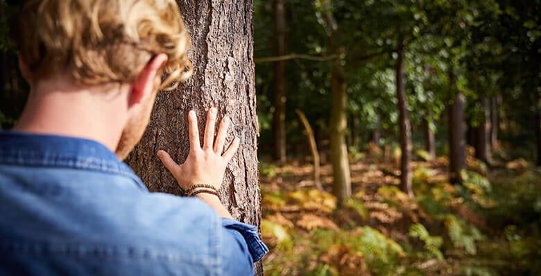 A man with his hand against the tree trunk in the forest